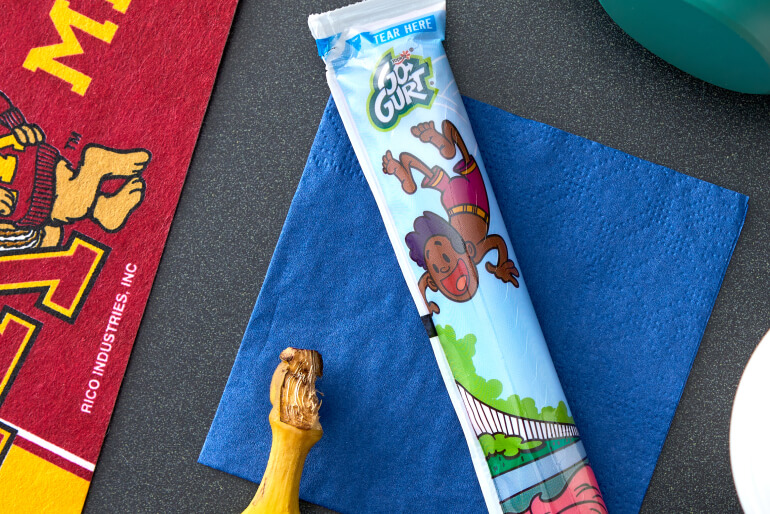 A Go-GURT tube sitting on a blue napkin on a tabletop beside a banana.