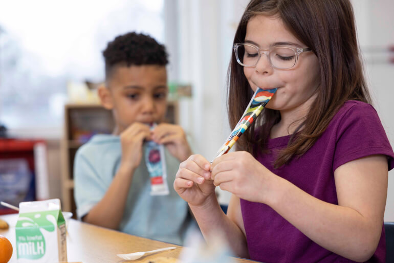 Two young children eating yogurt from Go-GURT tubes while sitting at a table.