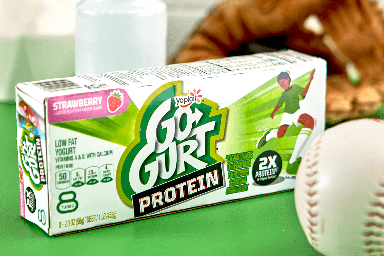 A box of strawberry Go-GURT Protein sitting on a green table beside a baseball.